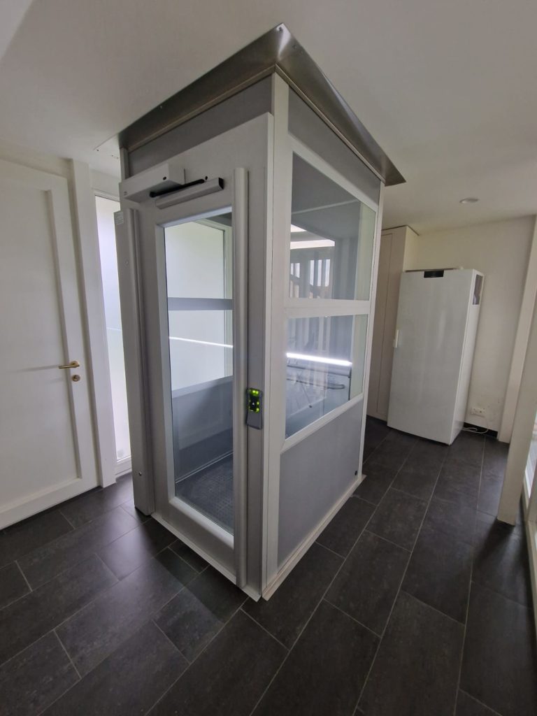 LSM Mobility Plateforme verticale fermée, cabine moderne avec parois vitrées, installée dans une pièce avec sol sombre. Élévateur domestique pour accessibilité.