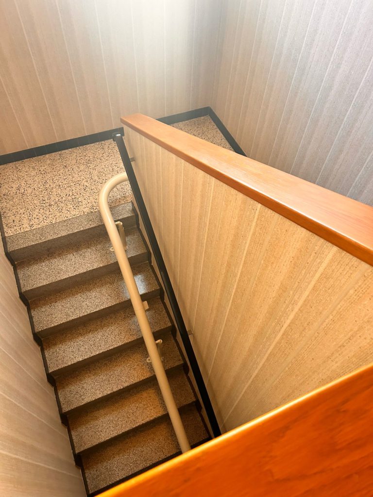 LSM Mobility Vue plongeante sur un escalier avec un siège monte-escaliers installé, mettant en avant une solution d'accessibilité dans un immeuble. Les marches en pierre et la rampe beige contrastent avec le mur texturé.
