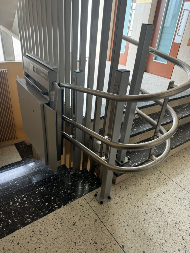 LSM Mobility Ascendor PLK8, plateforme monte-escaliers installée à Neuchâtel. La plateforme grise est repliée le long d'un escalier avec rampe métallique, sur un sol en damier noir et blanc.
