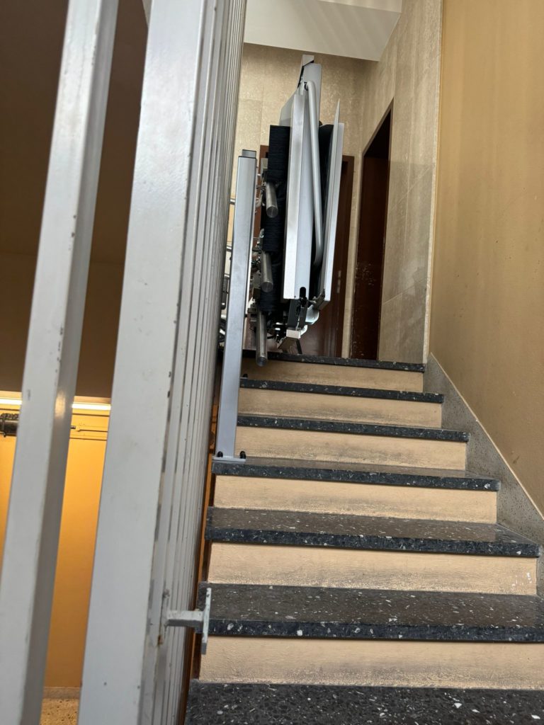 LSM Mobility Plateforme monte-escaliers Ascendor PLK8 installée dans une cage d'escalier. La plateforme est repliée, prête à l'emploi, sur des marches en béton noir et beige.