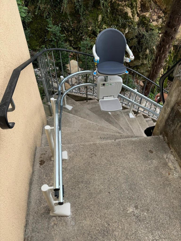 LSM Mobility Siège monte-escaliers installé sur un escalier extérieur en béton à Morges, avec un rail métallique courbé et un siège gris. Solution d'accessibilité pour domicile.