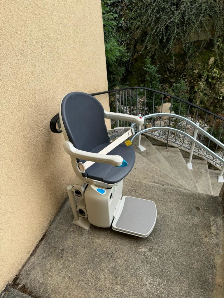 LSM Mobility Siège monte-escaliers installé dans la région de Morges, avec assise grise et rail longeant un escalier extérieur en béton. Végétation luxuriante en arrière-plan.