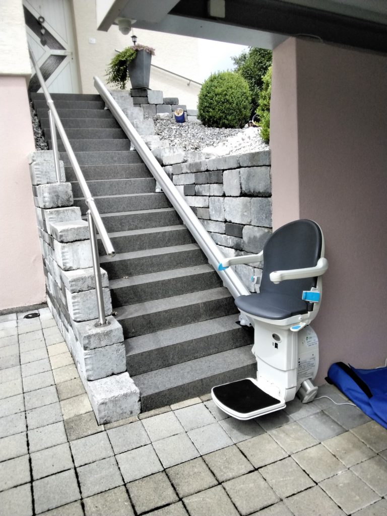 LSM Mobility Siège monte-escaliers extérieur installé sur un escalier en pierre menant à une maison. Le monte-escalier offre une solution d'accessibilité élégante et pratique.