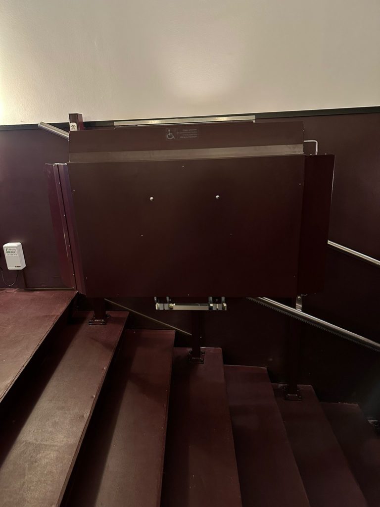 LSM Mobility Plateforme monte-escaliers marron installée dans le Cinéma Korso à Fribourg, assurant l'accessibilité aux personnes à mobilité réduite. L'escalier est également marron.