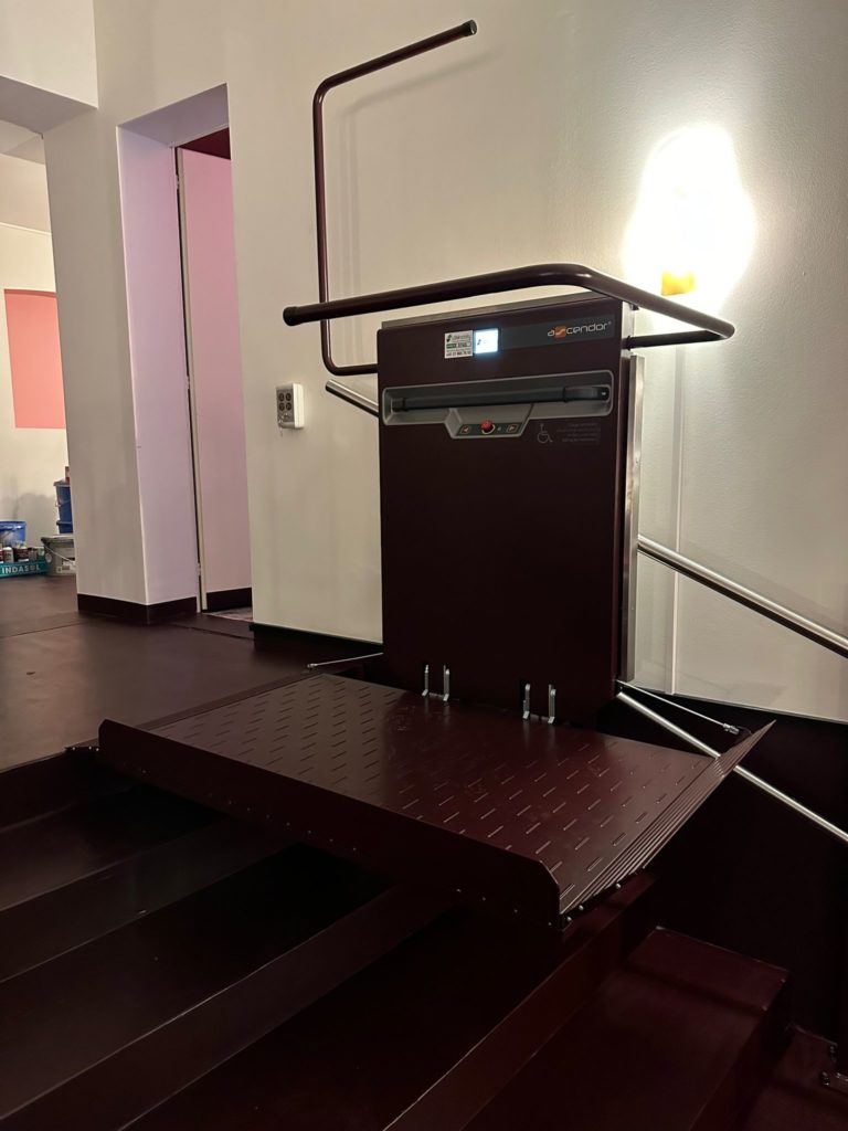 LSM Mobility Plateforme monte-escaliers Acorn installée au Cinéma Korso à Fribourg. L'élévateur marron foncé est replié, prêt à l'emploi. Rampe d'accès sur les marches. Sécurité et accessibilité.