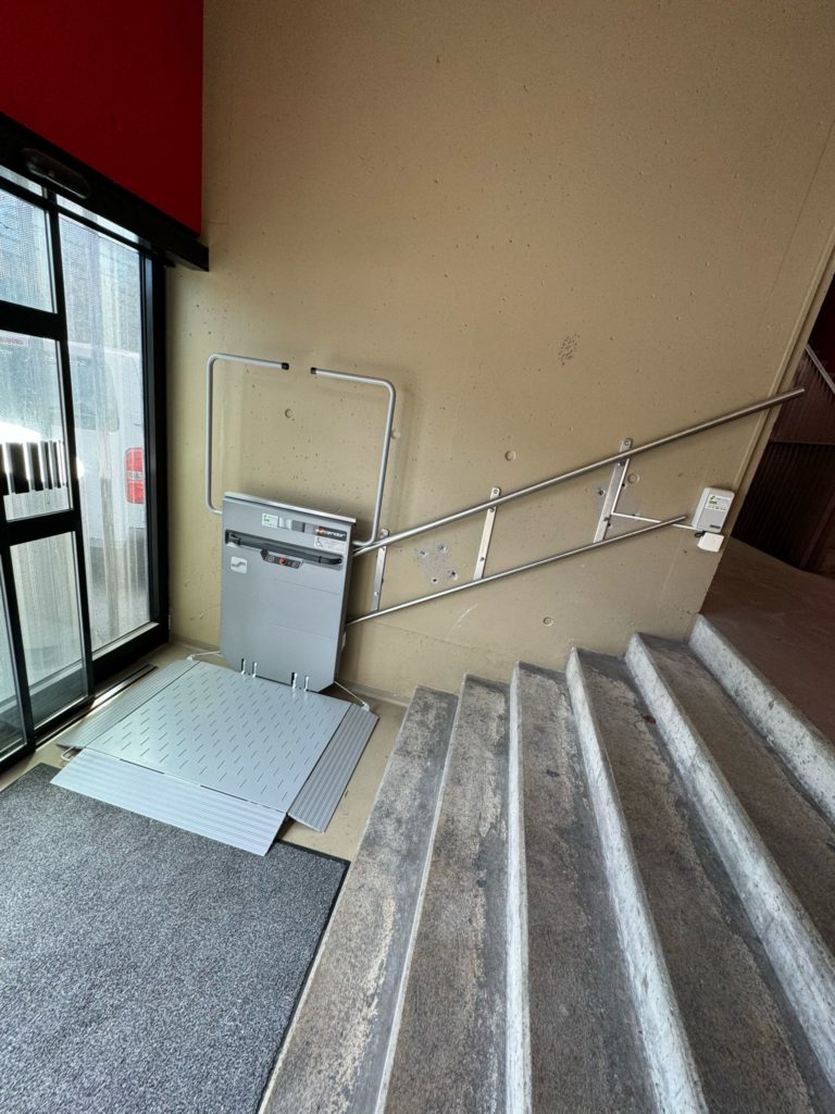 LSM Mobility Plateforme élévatrice installée près d'un escalier au stade de la Maladière à Neuchâtel. La plateforme grise contraste avec les marches en béton et le mur beige.
