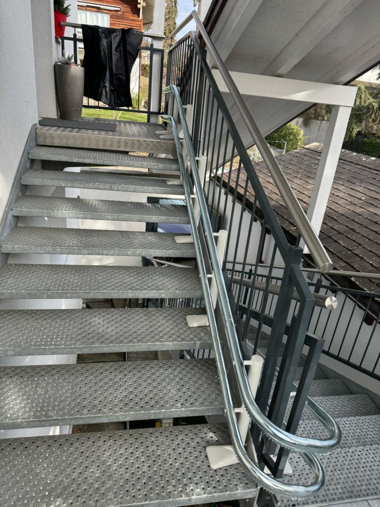LSM Mobility Escalier extérieur en métal avec un siège monte-escaliers Handicare 4000 installé. La rampe en acier inoxydable guide le regard vers le haut, dans un cadre résidentiel verdoyant.