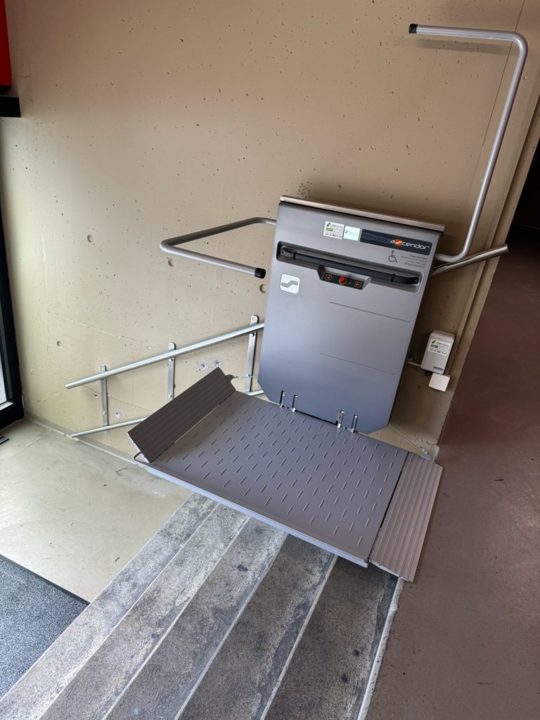 LSM Mobility Plateforme élévatrice pour fauteuil roulant installée dans les escaliers du stade de la Maladière à Neuchâtel. L'appareil gris clair est replié contre le mur, avec sa plateforme dépliée sur les marches.