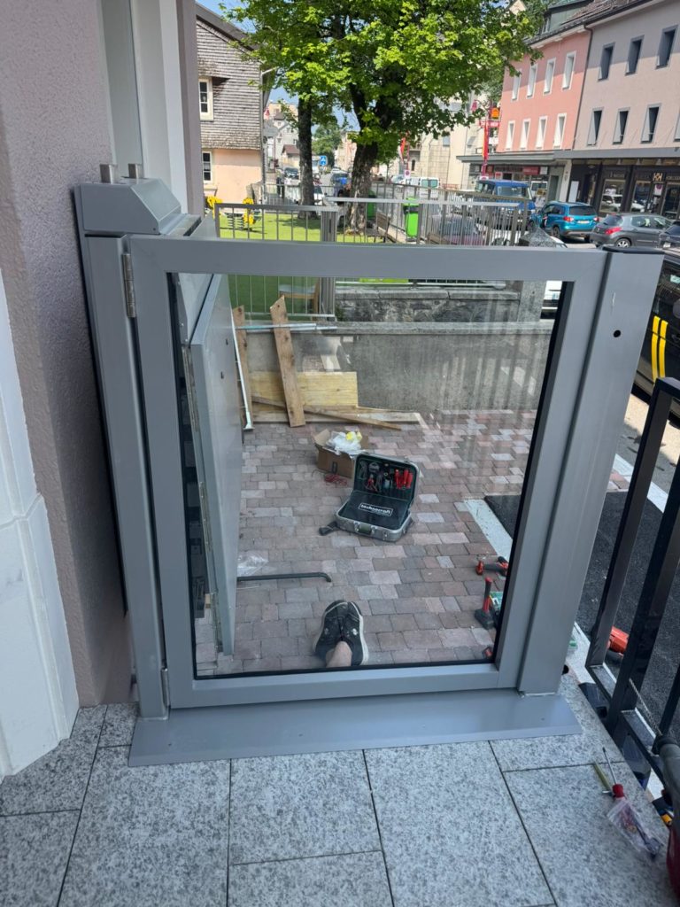 LSM Mobility Installation d'une plateforme élévatrice Ascendor PLV9 gris clair sur une terrasse pavée. Boîte à outils ouverte à proximité, suggérant un chantier en cours.