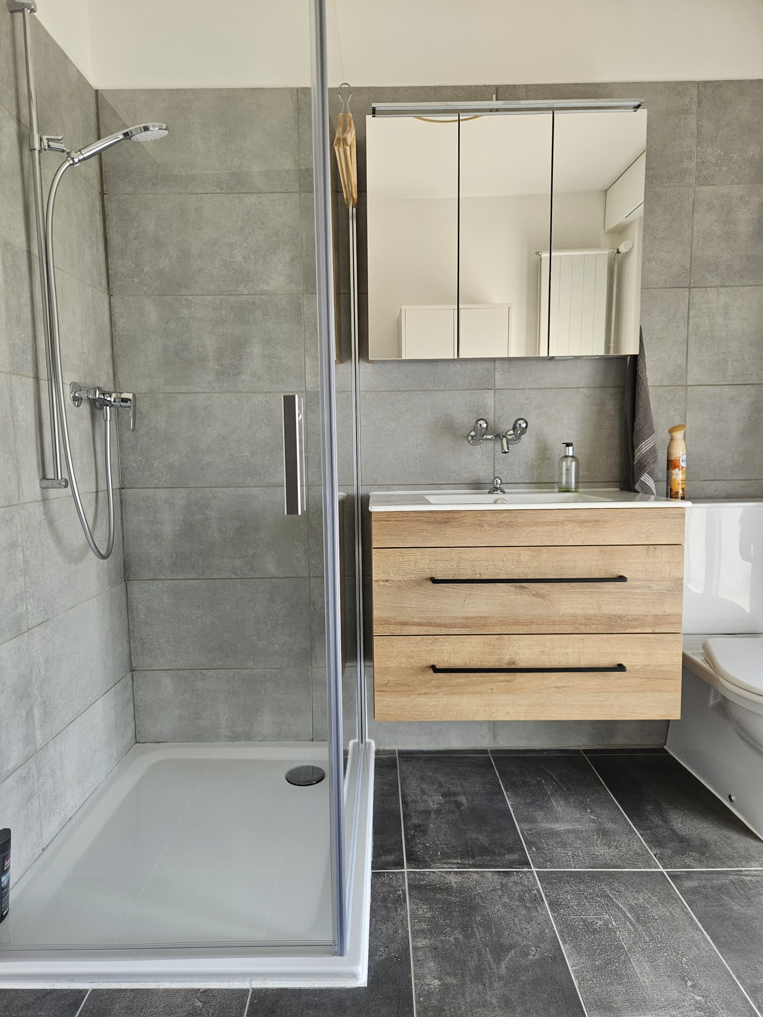 LSM Mobility Salle de bain moderne rénovée par LSM Mobility : douche à l'italienne, meuble vasque en bois clair, carrelage gris et sol foncé. Ambiance épurée et fonctionnelle.