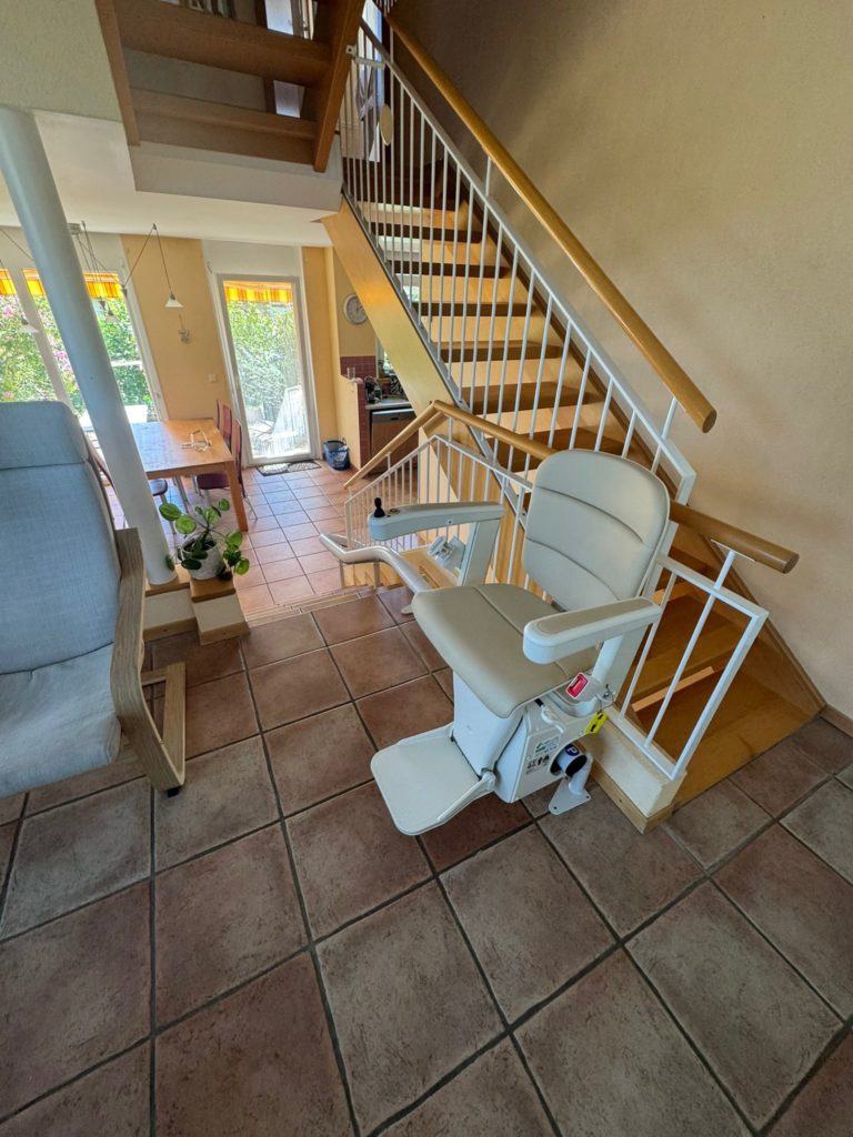 LSM Mobility Un monte-escalier beige installé sur un escalier en bois clair avec rampe blanche. Une salle à manger lumineuse est visible en arrière-plan.
