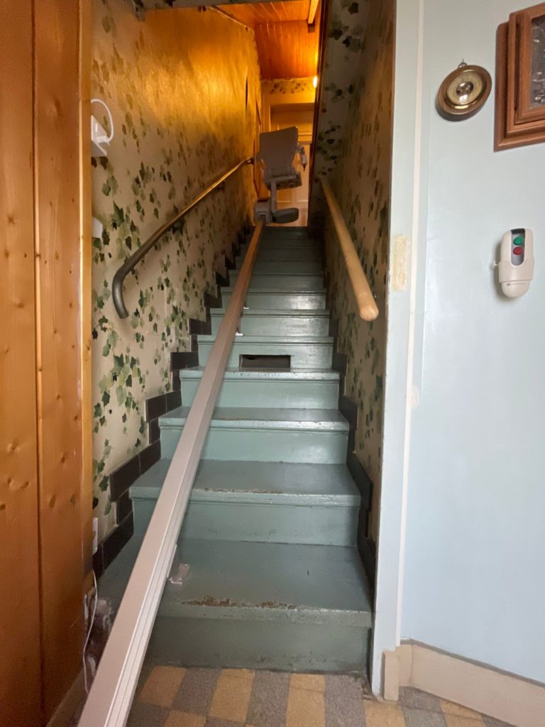 LSM Mobility Escalier intérieur avec monte-escalier, décor vintage et papier peint floral. Solution d'accessibilité pour maison à plusieurs étages.