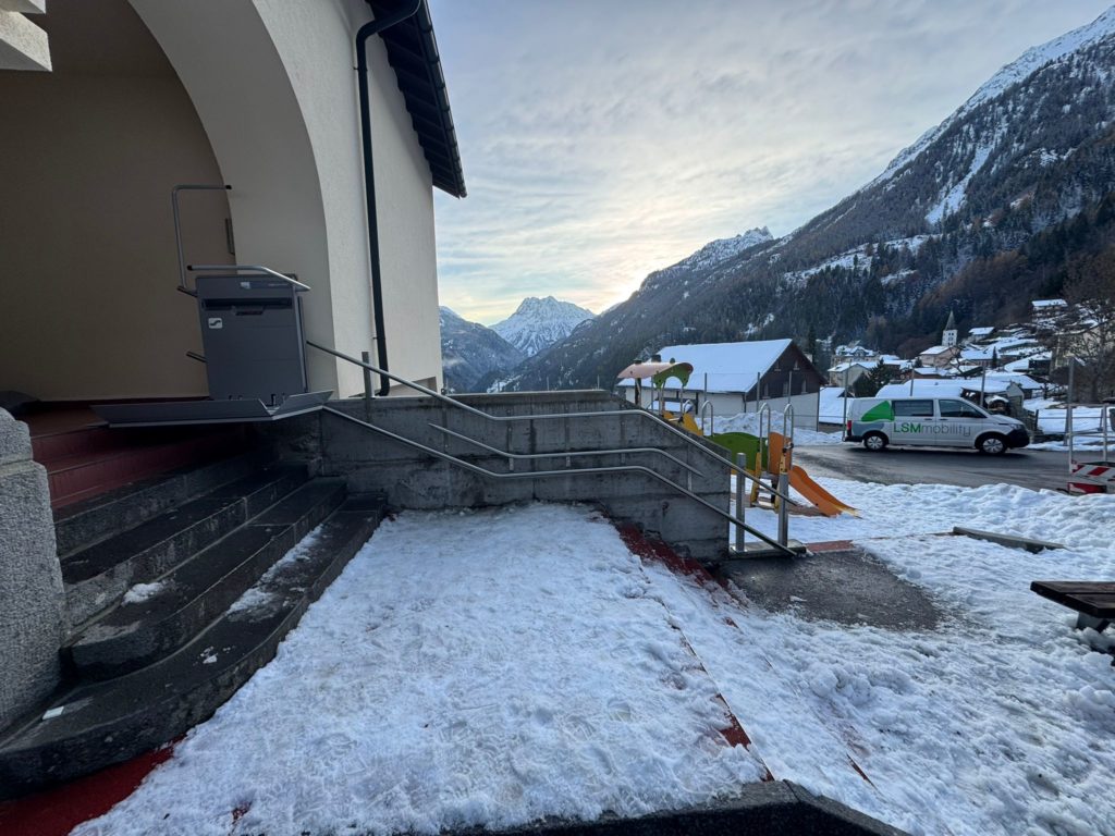 LSM Mobility Plateforme élévatrice installée dans la Vallée du Trient, devant un bâtiment enneigé avec vue sur les montagnes. Un véhicule "LSMobility" est visible à proximité.