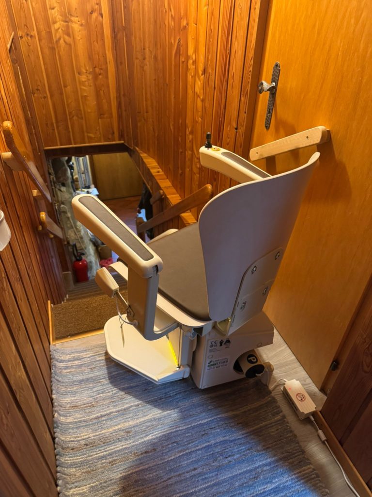 LSM Mobility Siège monte-escalier monorail installé dans un escalier en bois, offrant une solution d'accessibilité domestique. La chaise beige est repliée, prête à l'utilisation.