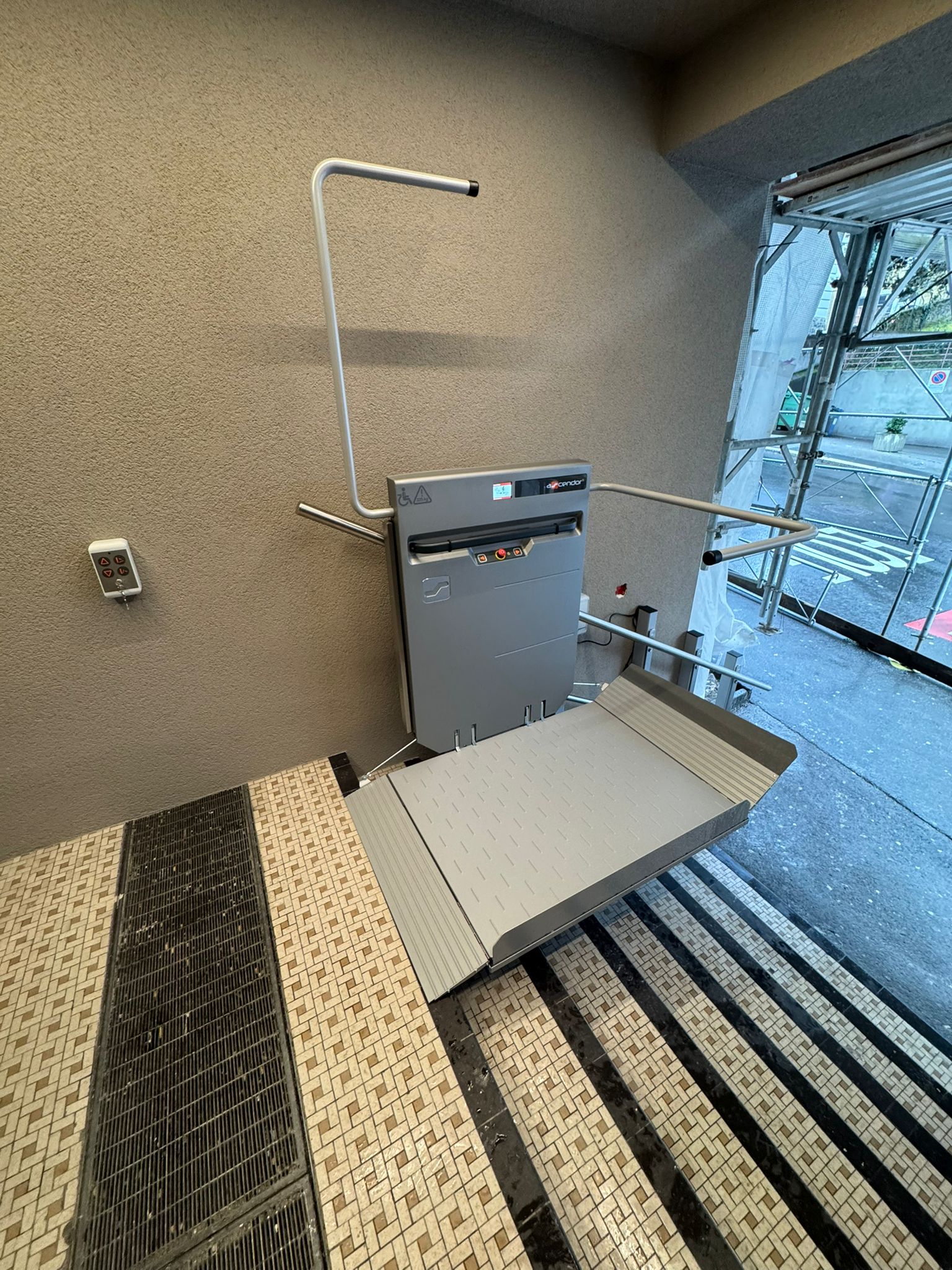 LSM Mobility Plateforme élévatrice PLG7 installée sur un escalier extérieur. La plateforme grise facilite l'accès aux personnes à mobilité réduite. Des travaux de construction sont visibles en arrière-plan.