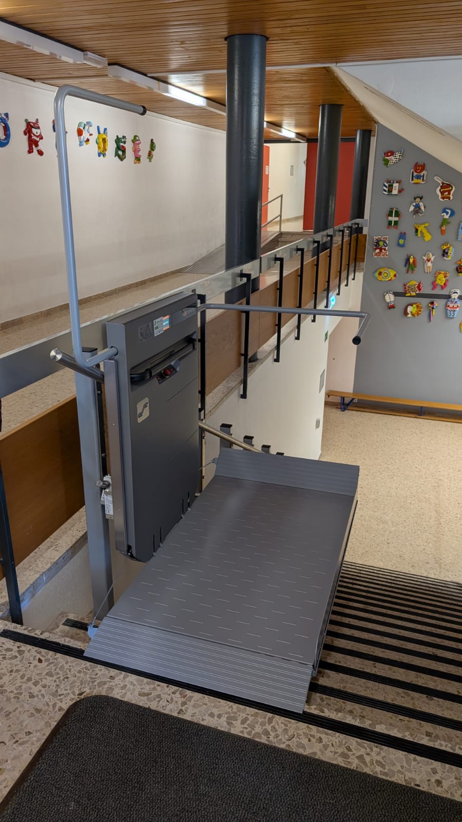 LSM Mobility Plateforme élévatrice grise installée dans un escalier d'école pour l'accessibilité. Le monte-escalier permet l'accès aux personnes à mobilité réduite. Des décorations enfantines ornent les murs.