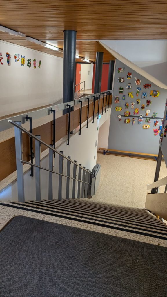 LSM Mobility Vue plongeante sur un escalier d'école avec des décorations murales colorées. L'image illustre l'accessibilité de l'école, avec des rampes et un tapis antidérapant.