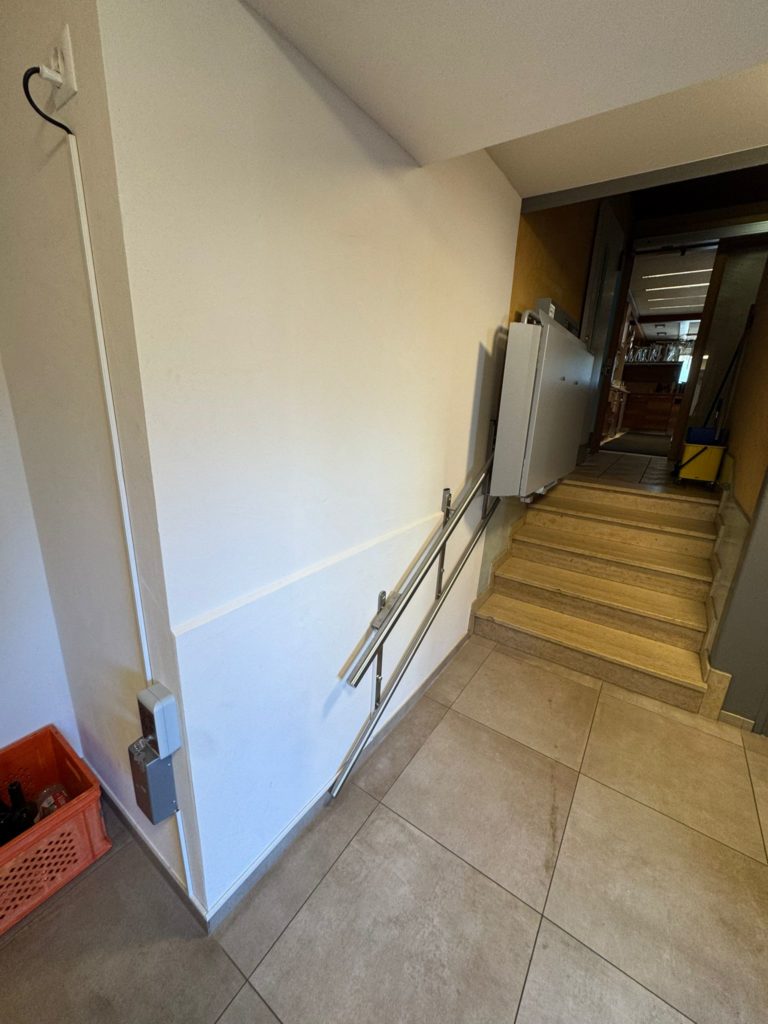 LSM Mobility Plateforme PLG7 installée près d'un escalier avec rampe. Élévateur pour personnes à mobilité réduite, intérieur clair et carrelé.