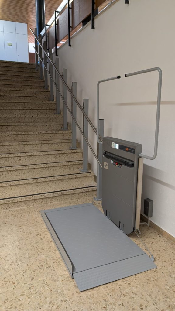 LSM Mobility Plateforme élévatrice grise installée à côté d'un escalier dans un bâtiment scolaire. Solution d'accessibilité pour les écoles, facilitant le déplacement des personnes à mobilité réduite.