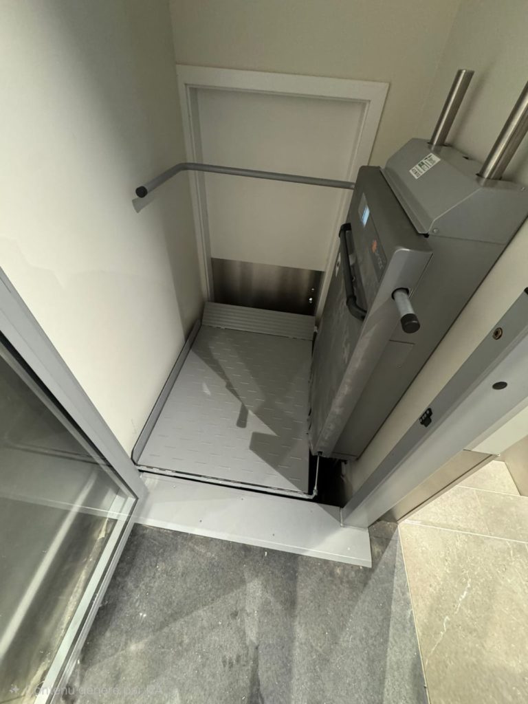 Monte-escalier plateforme gris installé dans un couloir étroit, avec rampe et porte. Accessibilité handicapé.