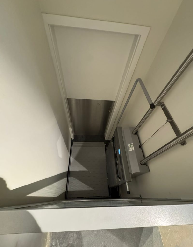 Plateforme élévatrice verticale pour fauteuil roulant avec rampe d'accès et porte blanche. Accessibilité handicapé.