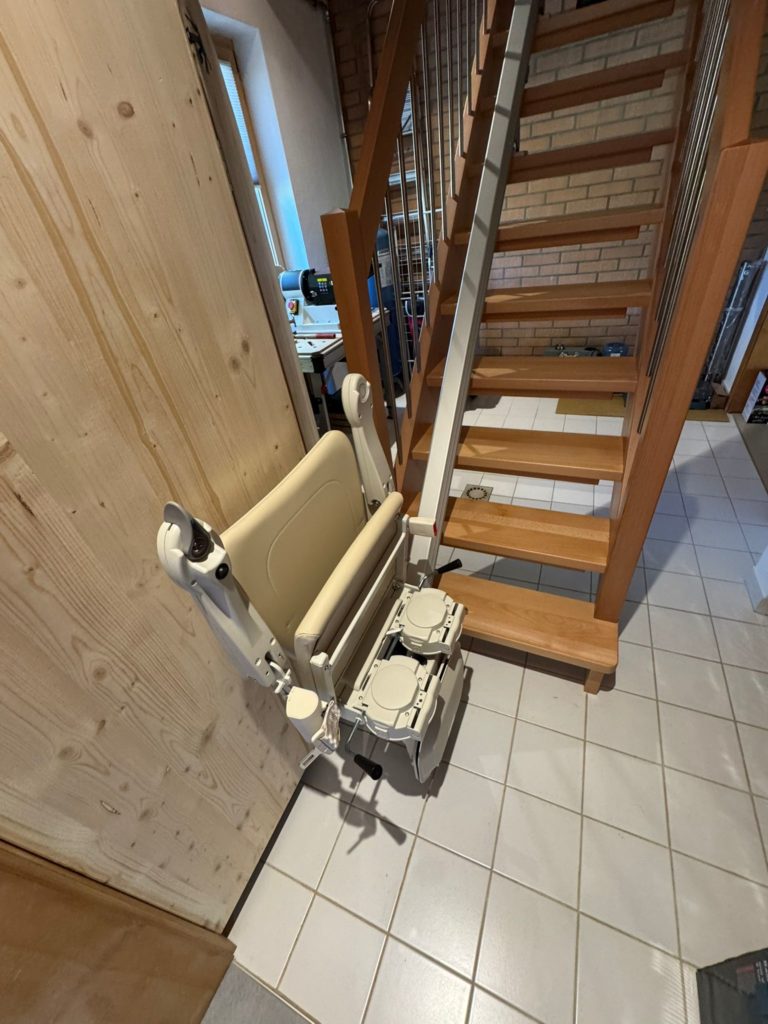 LSM Mobility Siège monte-escalier beige replié le long d'un mur en bois près d'un escalier