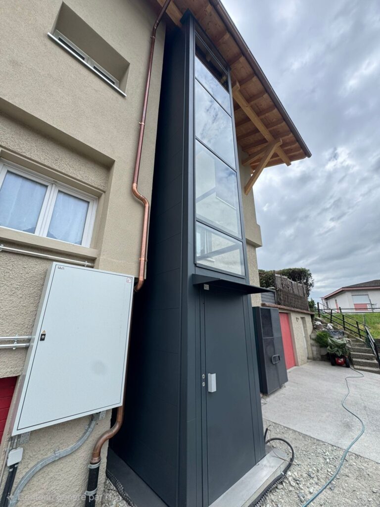 LSM Mobility Ascenseur extérieur vitré gris installé sur le mur d'une maison beige.