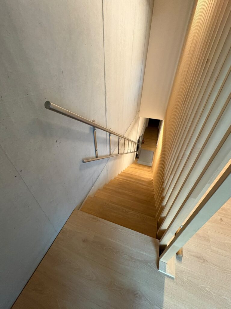 LSM Mobility Escalier en bois moderne avec rampe en métal et mur en béton brut.