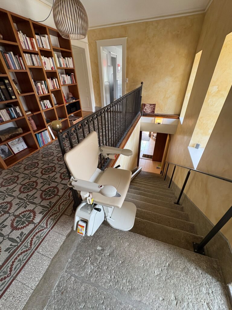 LSM Mobility Fauteuil monte-escalier beige installé dans un escalier en pierre avec bibliothèque
