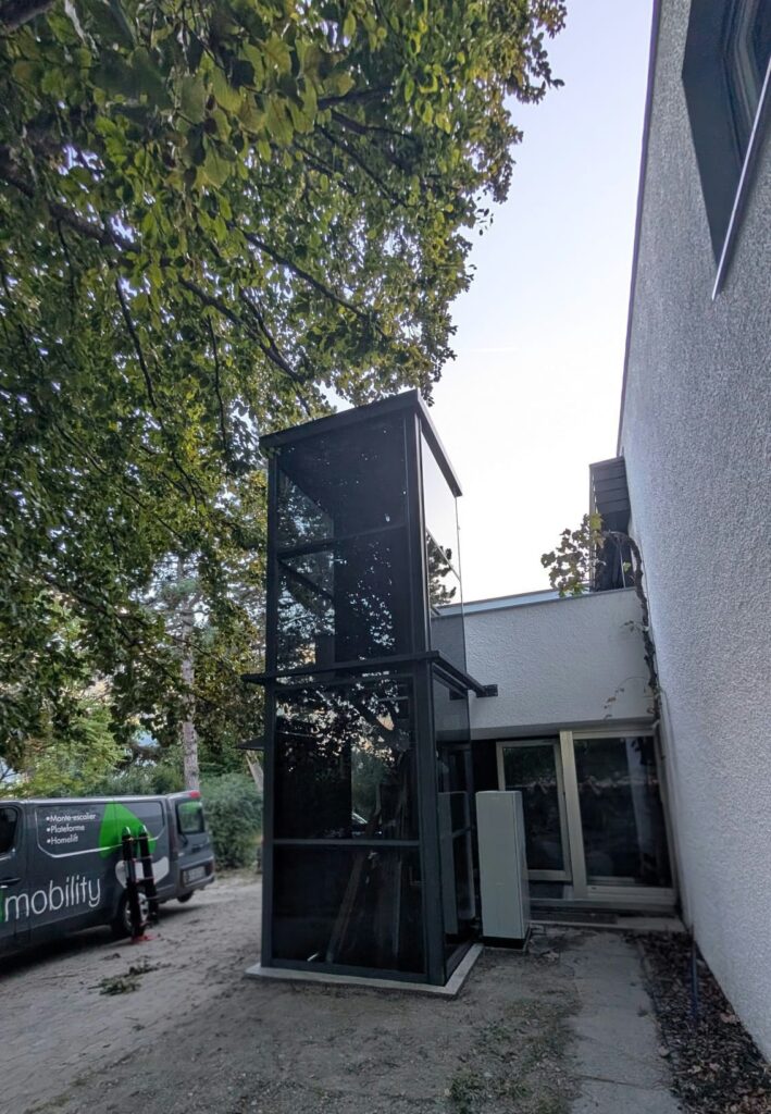 LSM Mobility Ascenseur extérieur vitré pour accessibilité, installé près d'un bâtiment.