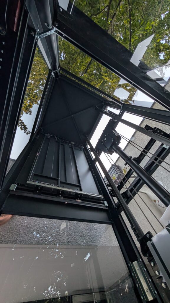 LSM Mobility Ascenseur extérieur en métal noir avec cabine vitrée vue de dessous.