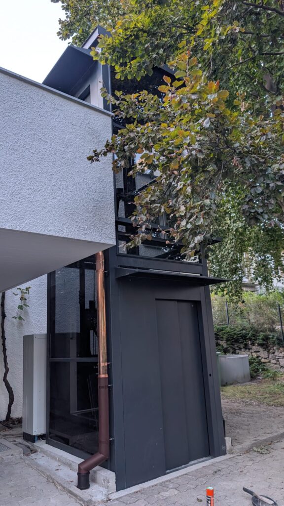 LSM Mobility Ascenseur extérieur moderne en noir et cuivre devant une maison blanche