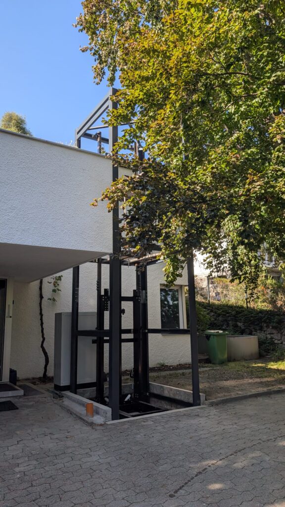 LSM Mobility Plateforme élévatrice extérieure installée devant un bâtiment blanc, près d'un arbre feuillu